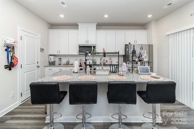 kitchen with a kitchen breakfast bar, a center island with sink, white cabinetry, and stainless steel appliances