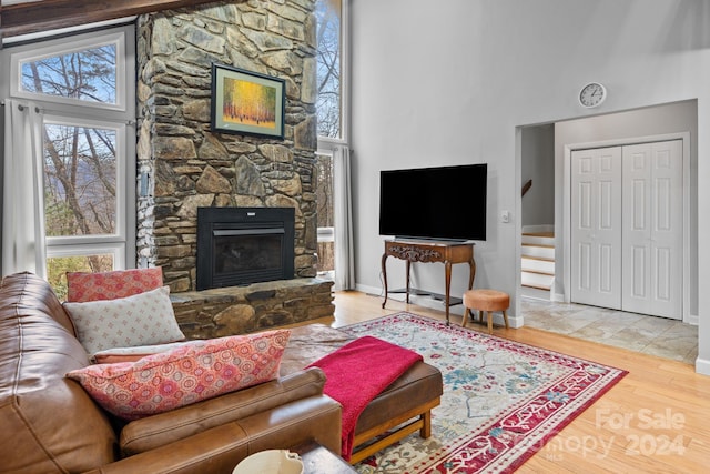 living room with hardwood / wood-style flooring, a stone fireplace, and a high ceiling