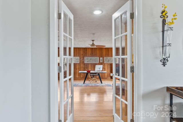 corridor featuring wood-type flooring, wooden walls, and french doors