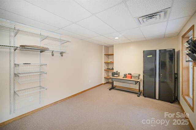 basement featuring black refrigerator, carpet, and a drop ceiling