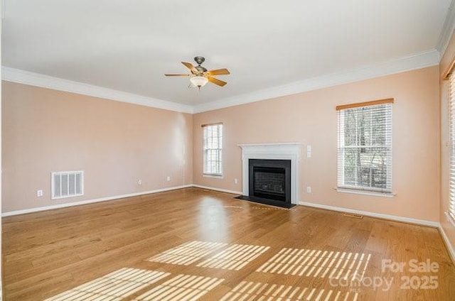 unfurnished living room featuring visible vents, crown molding, baseboards, and wood finished floors