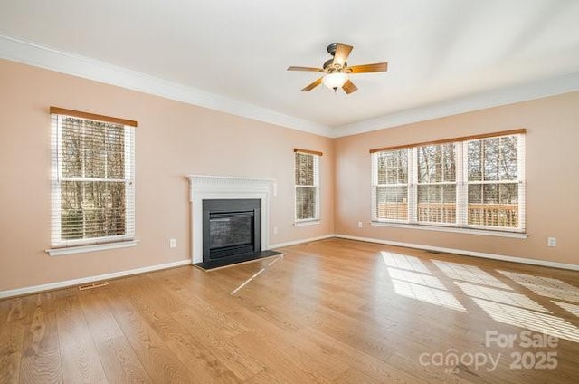 unfurnished living room featuring baseboards, ornamental molding, wood finished floors, and a glass covered fireplace