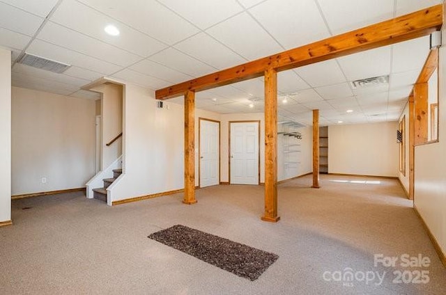 finished below grade area with a paneled ceiling, visible vents, stairway, and carpet flooring