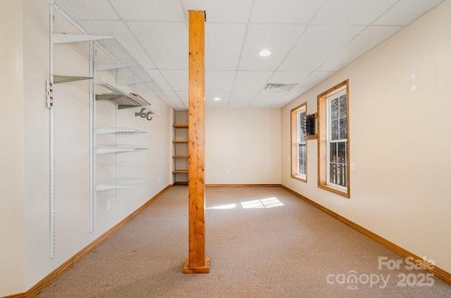 below grade area with visible vents, carpet, a paneled ceiling, and baseboards