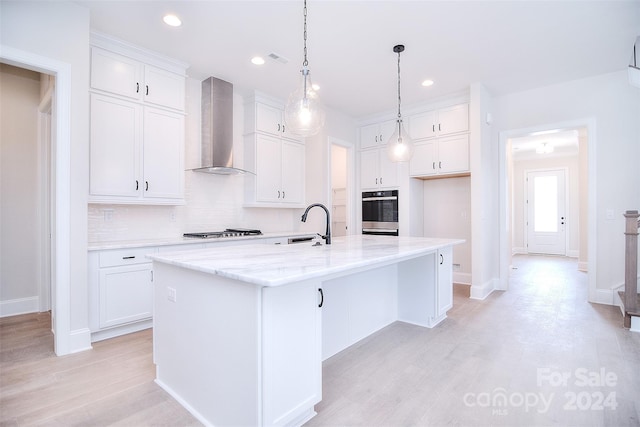 kitchen featuring tasteful backsplash, a center island with sink, white cabinets, and wall chimney range hood