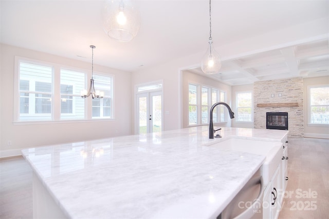 kitchen with white cabinets, coffered ceiling, open floor plan, light stone countertops, and pendant lighting