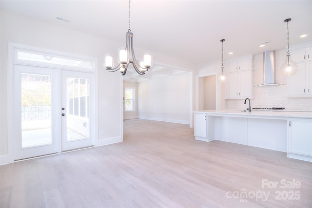 kitchen featuring light countertops, wall chimney range hood, white cabinetry, and pendant lighting