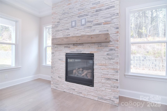 interior details featuring ornamental molding, a fireplace, baseboards, and wood finished floors