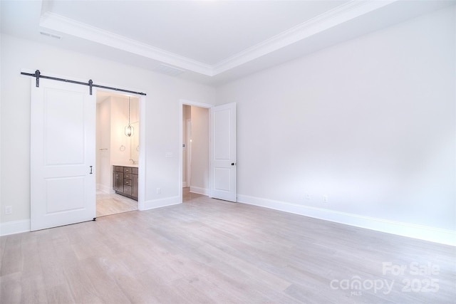 unfurnished bedroom with a barn door, visible vents, baseboards, ornamental molding, and light wood-style floors