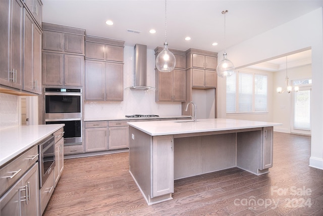 kitchen featuring a kitchen island with sink, pendant lighting, wall chimney range hood, and appliances with stainless steel finishes