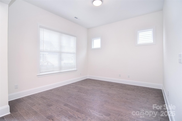 empty room featuring visible vents, baseboards, and dark wood finished floors