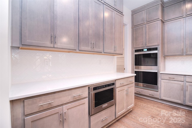 kitchen with double oven, light countertops, light wood-style flooring, and tasteful backsplash