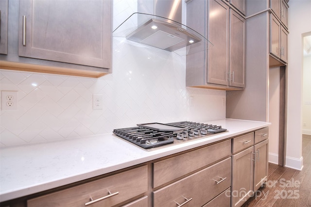 kitchen with wall chimney exhaust hood, light countertops, dark wood finished floors, and stainless steel gas stovetop