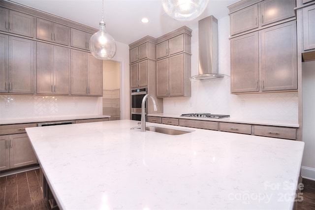 kitchen featuring dark wood finished floors, an island with sink, appliances with stainless steel finishes, wall chimney range hood, and a sink