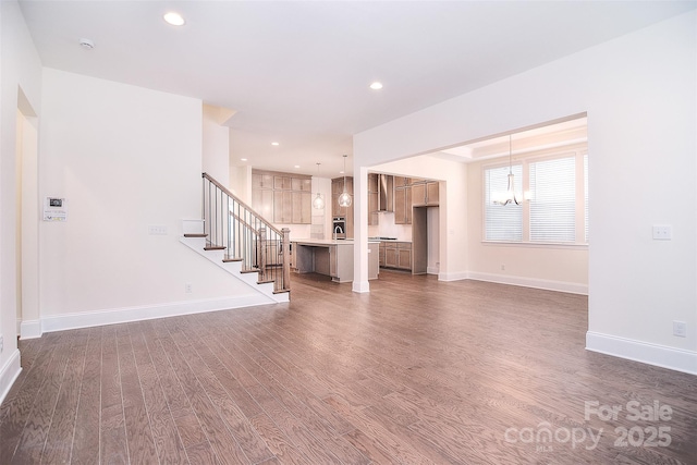 unfurnished living room featuring a chandelier, wood finished floors, baseboards, and stairs