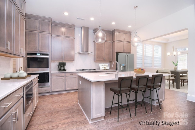 kitchen featuring wood finished floors, visible vents, wall chimney range hood, appliances with stainless steel finishes, and tasteful backsplash