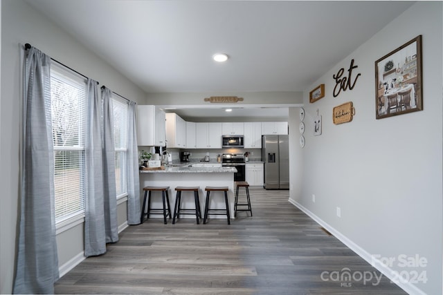 kitchen featuring kitchen peninsula, a kitchen bar, stainless steel appliances, sink, and white cabinetry