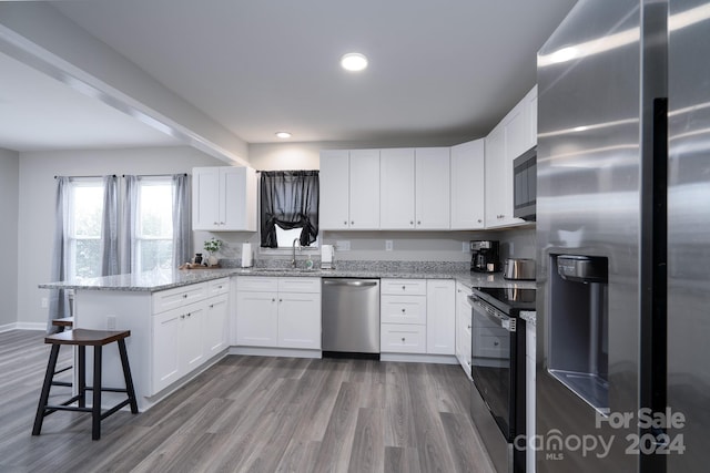 kitchen featuring sink, kitchen peninsula, appliances with stainless steel finishes, light stone counters, and white cabinetry