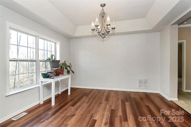 unfurnished dining area featuring a raised ceiling, a notable chandelier, and dark wood-type flooring