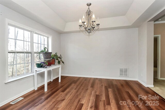 unfurnished dining area featuring dark hardwood / wood-style floors, a chandelier, a raised ceiling, and a healthy amount of sunlight