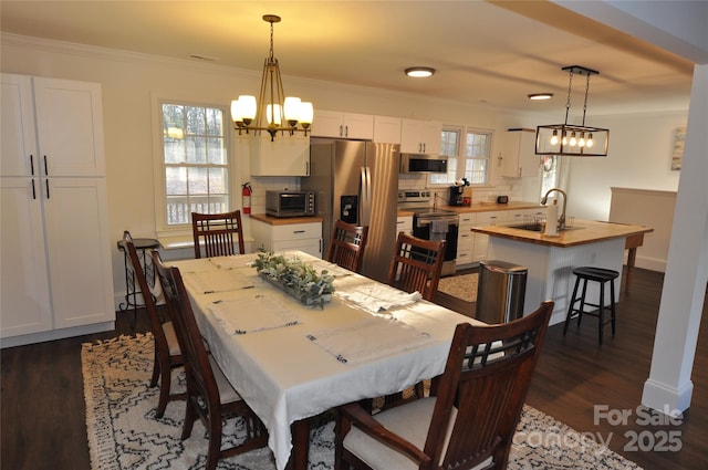 dining area with dark hardwood / wood-style floors, crown molding, sink, and a chandelier