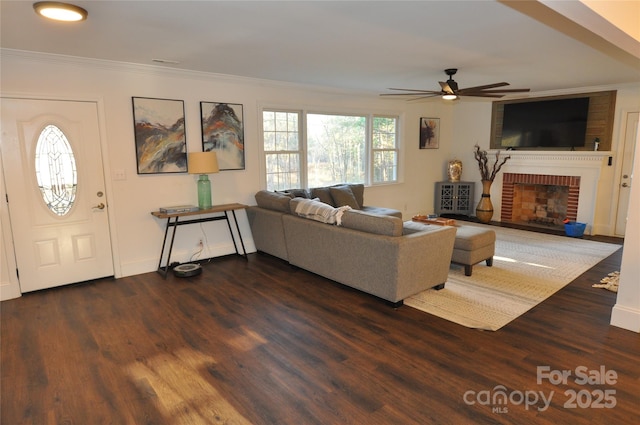 living room featuring a fireplace, crown molding, ceiling fan, and dark wood-type flooring