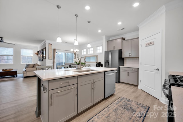 kitchen featuring appliances with stainless steel finishes, gray cabinetry, sink, a center island with sink, and decorative light fixtures