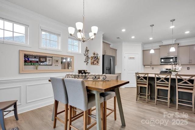 dining space featuring ornamental molding, light wood-type flooring, and a notable chandelier