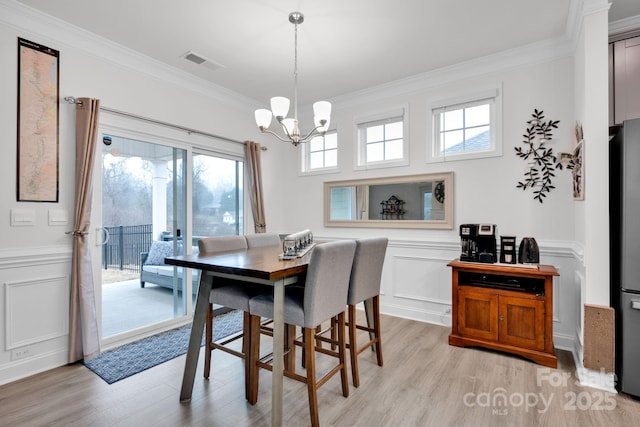 dining space with crown molding, light hardwood / wood-style flooring, and an inviting chandelier