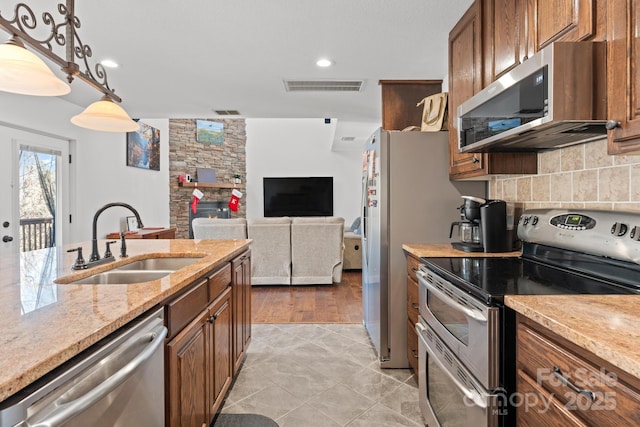 kitchen with appliances with stainless steel finishes, sink, decorative backsplash, hanging light fixtures, and light stone counters