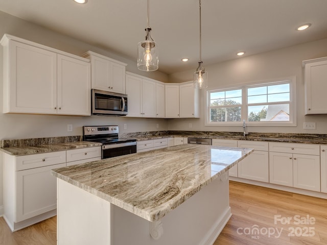 kitchen with light stone countertops, white cabinetry, pendant lighting, a kitchen island, and appliances with stainless steel finishes