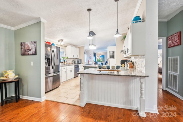 kitchen with kitchen peninsula, stainless steel refrigerator with ice dispenser, hanging light fixtures, tasteful backsplash, and white cabinetry