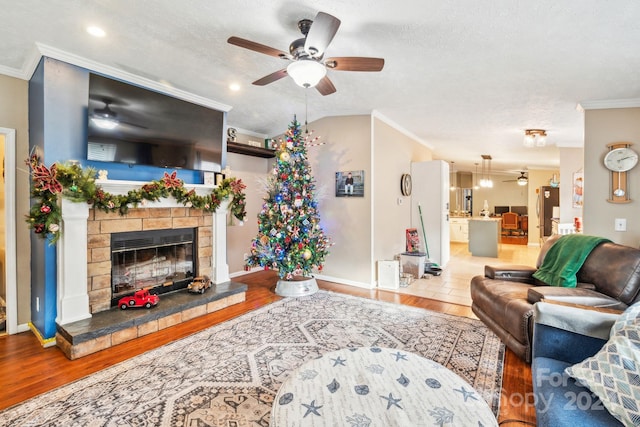 living room featuring a textured ceiling, a stone fireplace, wood-type flooring, and crown molding