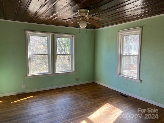 empty room featuring a wealth of natural light, dark hardwood / wood-style flooring, ceiling fan, and wooden ceiling