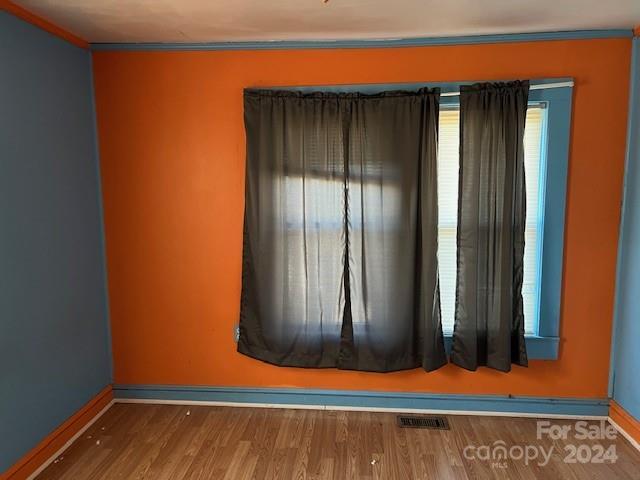 spare room featuring wood-type flooring and crown molding