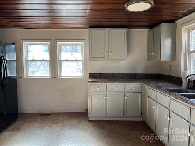 kitchen featuring white cabinets, black fridge, sink, and a wealth of natural light