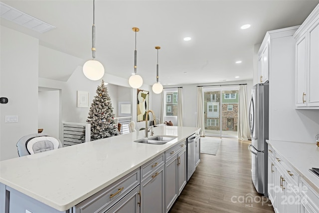 kitchen with white cabinetry, sink, stainless steel appliances, pendant lighting, and a center island with sink