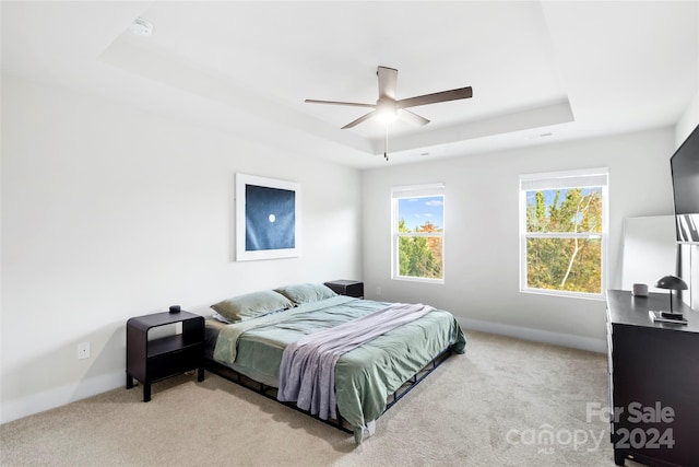 bedroom featuring ceiling fan, a raised ceiling, and light carpet