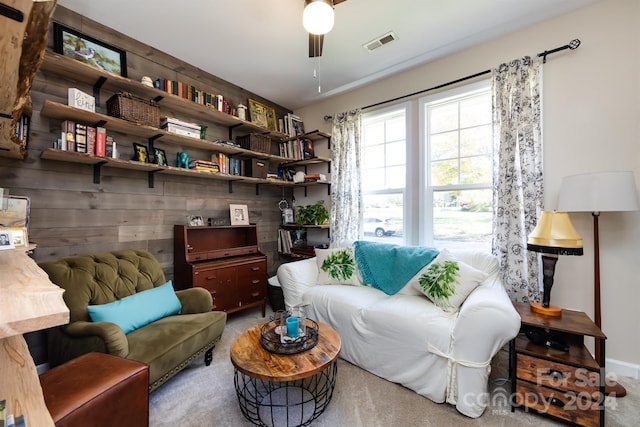 sitting room with wood walls, carpet, and ceiling fan