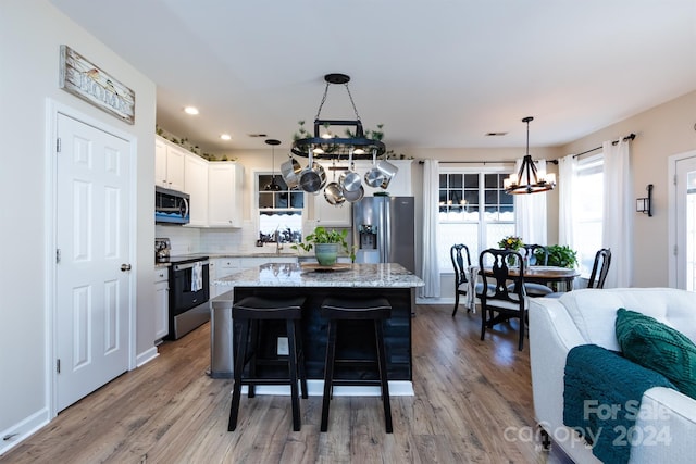 kitchen featuring white cabinetry, a center island, light hardwood / wood-style floors, decorative light fixtures, and appliances with stainless steel finishes