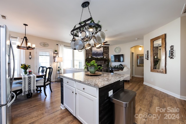 kitchen with stainless steel fridge, light stone countertops, a kitchen island, white cabinetry, and a chandelier