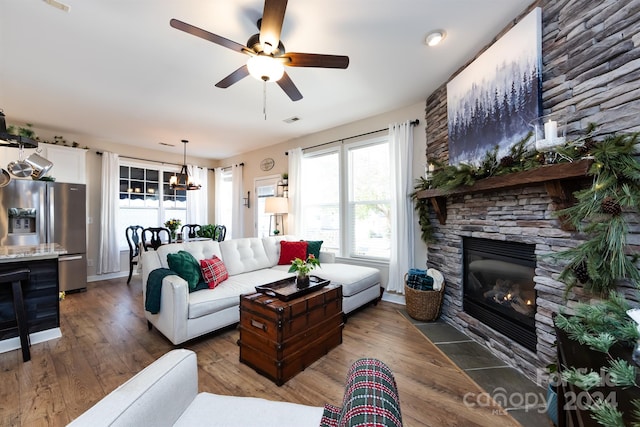 living room with a fireplace, dark wood-type flooring, and ceiling fan with notable chandelier