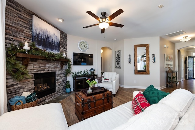 living room with ceiling fan, dark hardwood / wood-style floors, and a stone fireplace