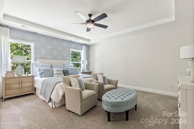 carpeted bedroom with ceiling fan, multiple windows, and a tray ceiling