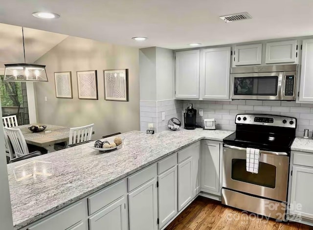 kitchen with hardwood / wood-style floors, white cabinets, hanging light fixtures, appliances with stainless steel finishes, and light stone counters