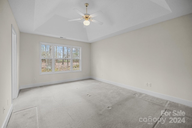 empty room featuring ceiling fan, a raised ceiling, and light colored carpet