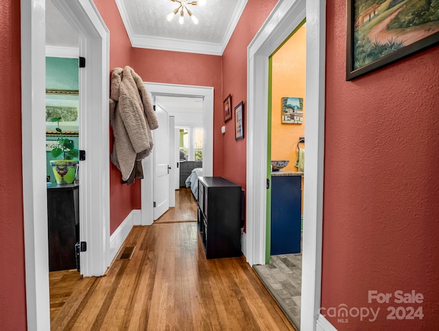 hall with wood-type flooring, a textured ceiling, ornamental molding, and a notable chandelier