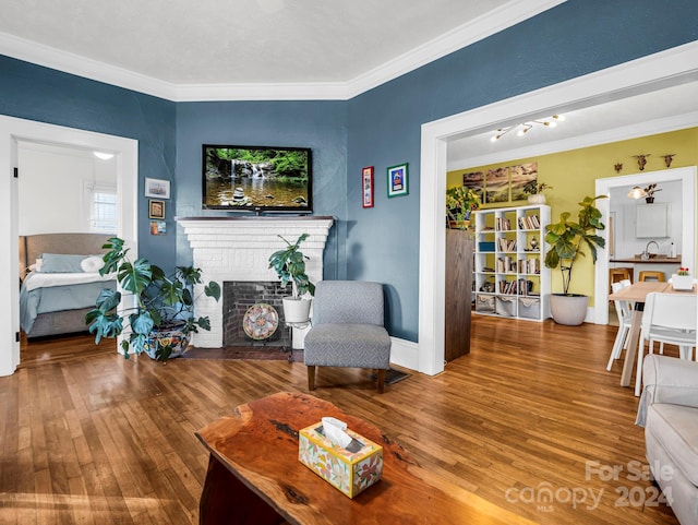 living room with hardwood / wood-style flooring, sink, ornamental molding, and a brick fireplace