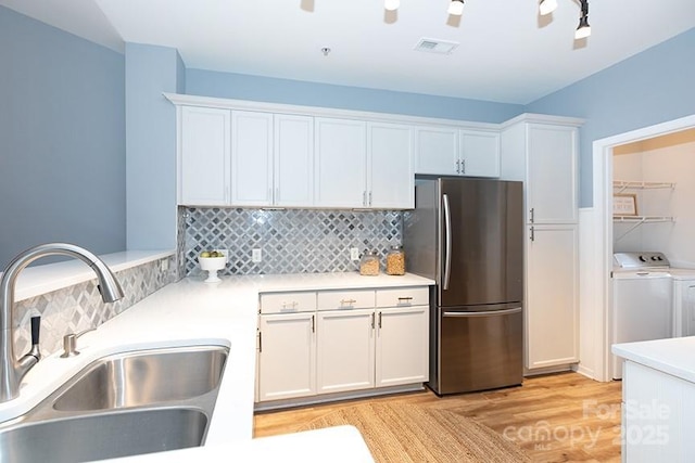 kitchen featuring freestanding refrigerator, white cabinets, a sink, and separate washer and dryer