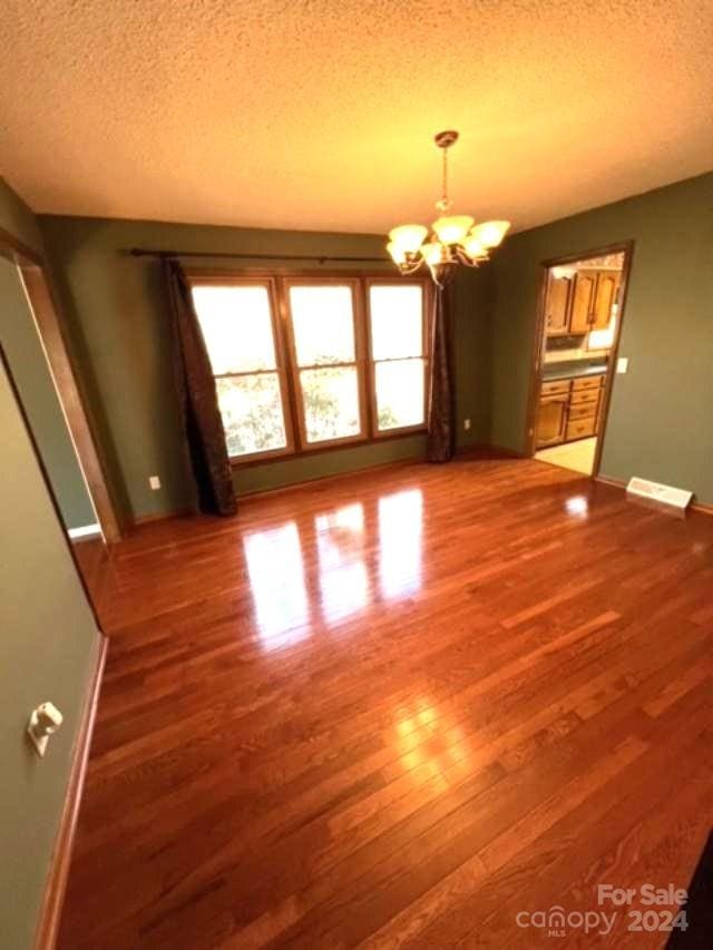 spare room featuring wood-type flooring, a textured ceiling, and an inviting chandelier